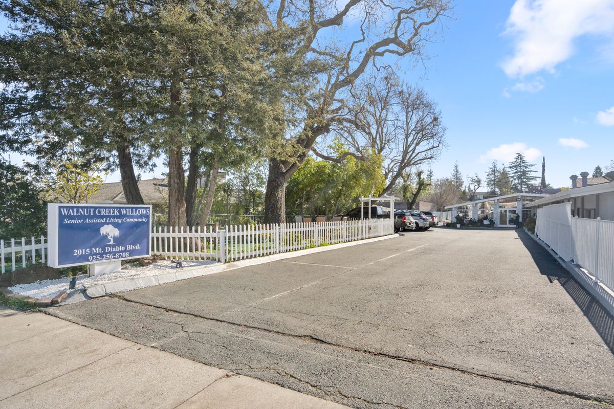 A parking lot surrounded by trees and a fence, with several cars parked during the daytime.