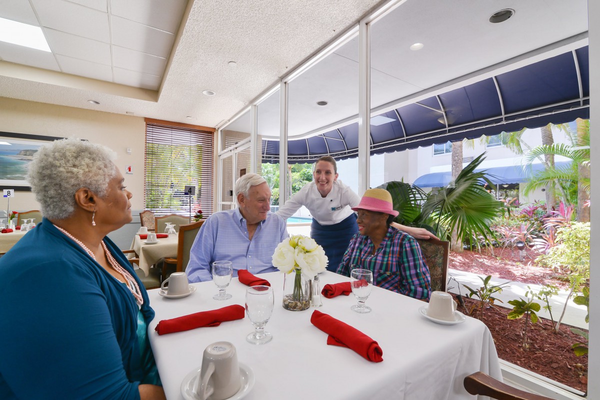 A group of seniors enjoying a meal together at a restaurant, attended by a waitress.