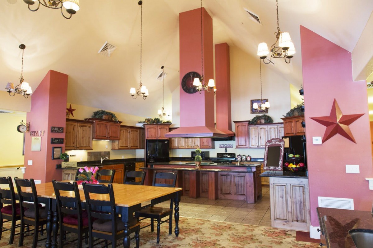 A spacious kitchen with high ceilings and wooden cabinetry, featuring a central island and a dining area.