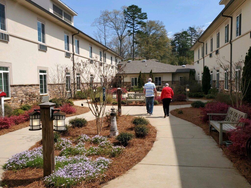 Two people walking along a landscaped courtyard pathway between buildings.