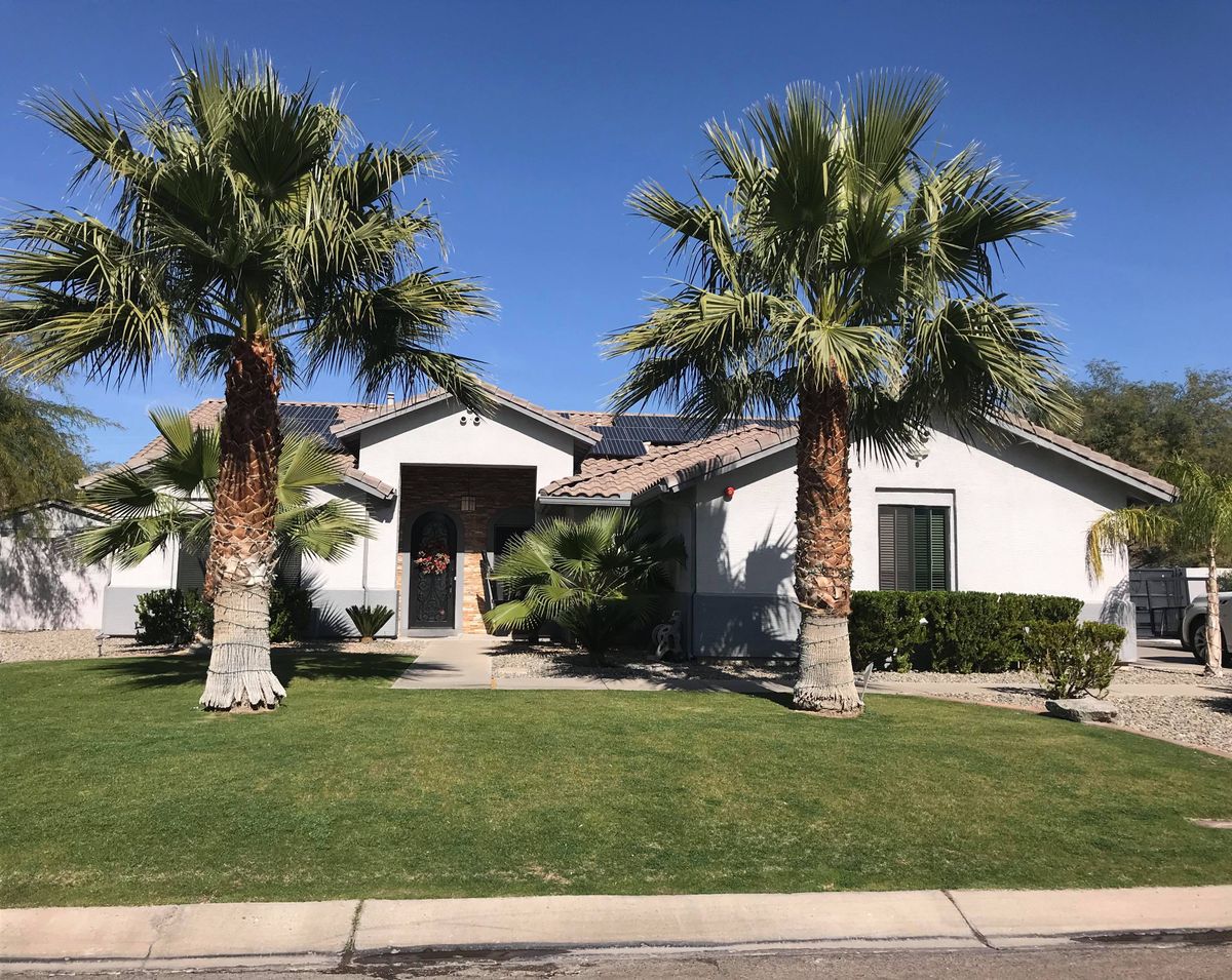 A suburban house with well-maintained landscaping and palm trees under a clear blue sky.