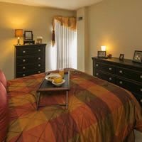 A cozy bedroom with warm lighting, featuring a neatly made bed and dark wood dressers.