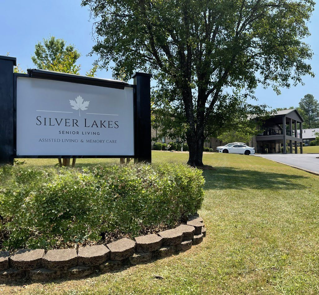 Sign for Silver Lake Apartments near a tree and lawn, with a building in the background.