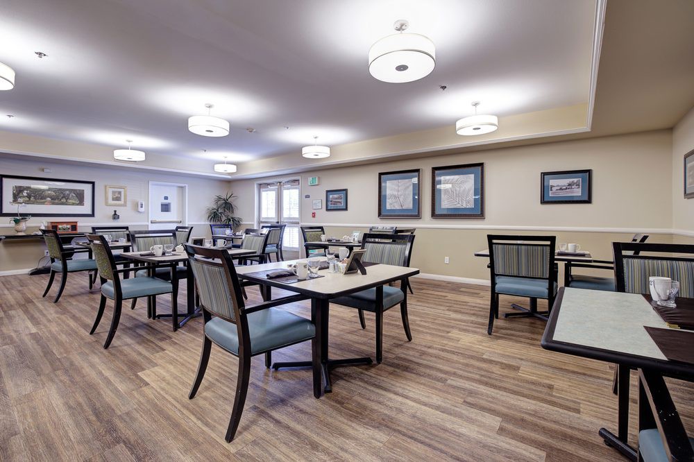 A modern dining room with neatly arranged tables and chairs, featuring warm lighting and wooden flooring.