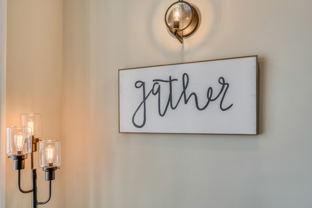 A cozy interior with a 'gather' wall sign and warm lighting.