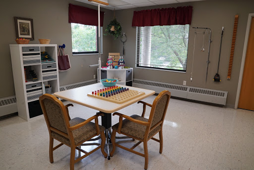 A cozy recreational space featuring a table with colorful toys and comfortable chairs, illuminated by natural light from the windows.
