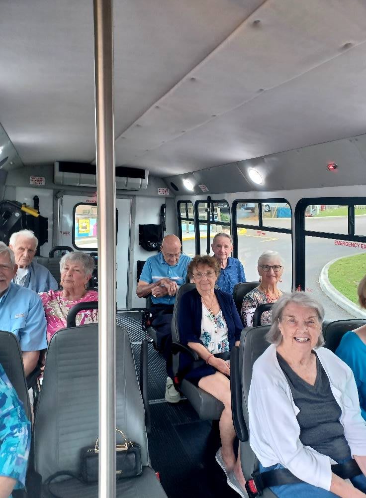 A group of elderly passengers smiling while riding on a bus.