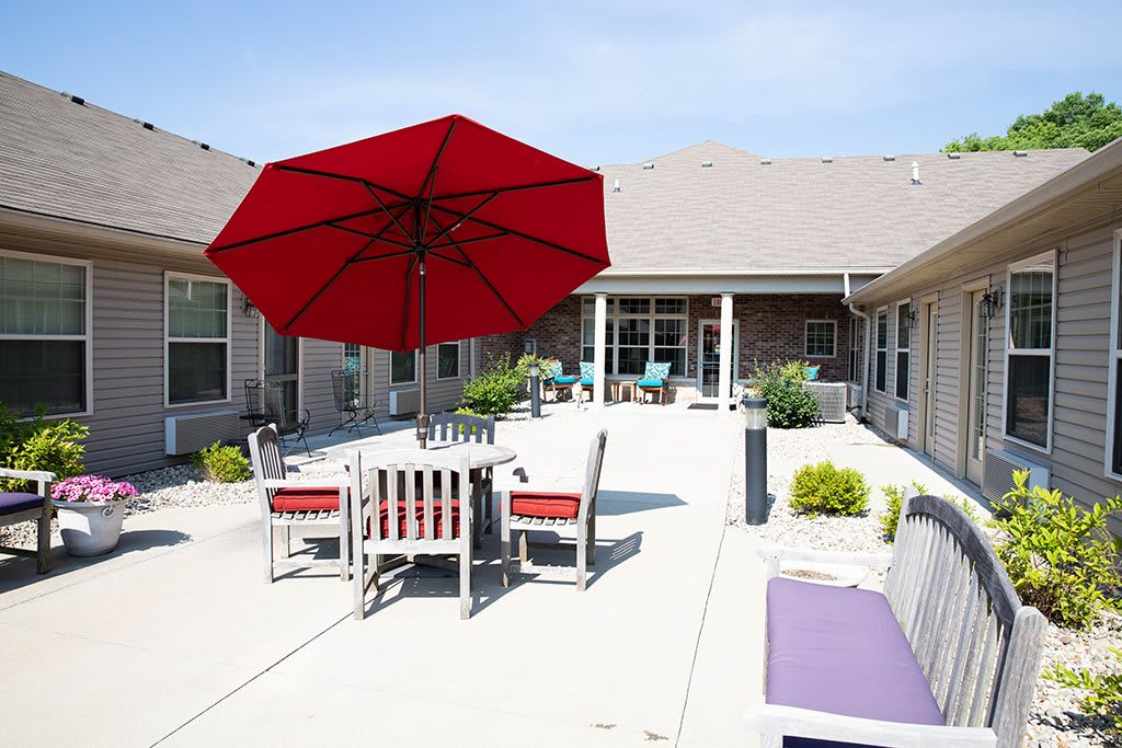 A sunny patio with a red umbrella and outdoor seating area.