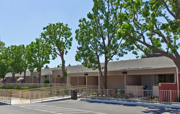 A view of a building with trees and a parking lot in the foreground.