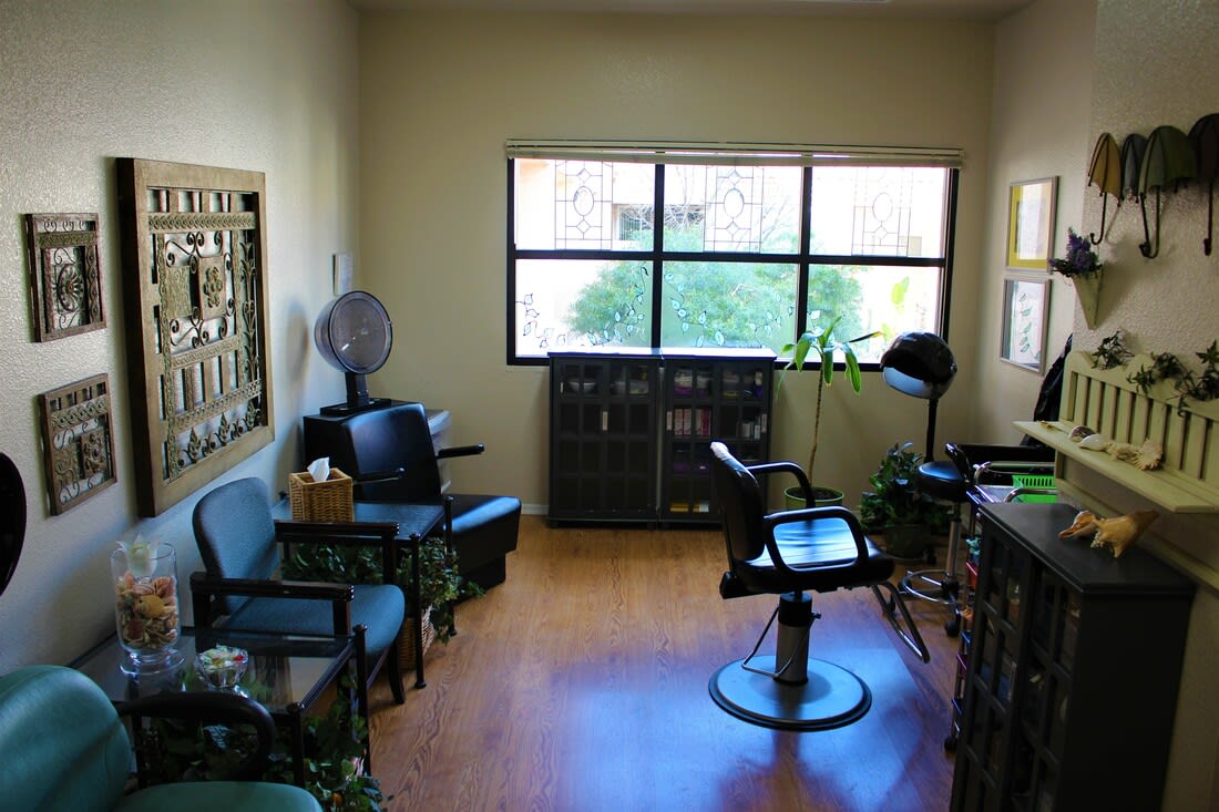 A cozy salon interior featuring a barber chair, seating for clients, and a large window providing natural light.