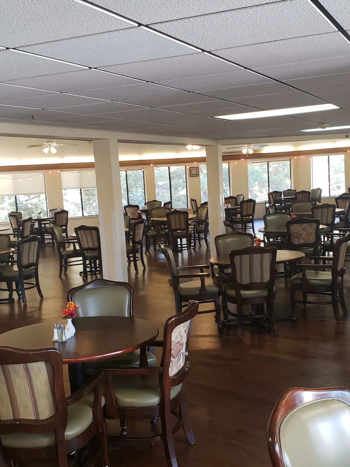 An empty dining area with multiple tables and chairs, featuring a wooden floor and natural lighting.