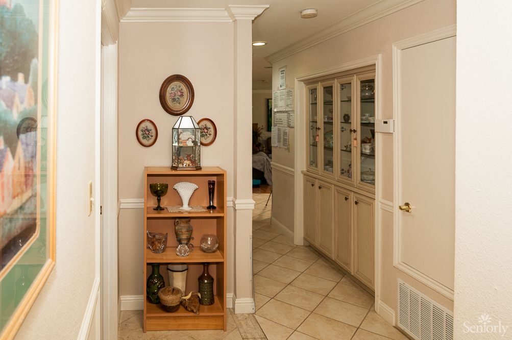 A cozy hallway featuring a wooden shelf adorned with decorative ceramics and frames, leading to a built-in cabinet along the wall.