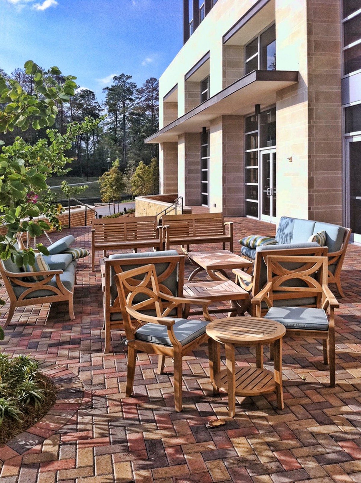 A modern outdoor patio area featuring wooden furniture and surrounded by greenery.