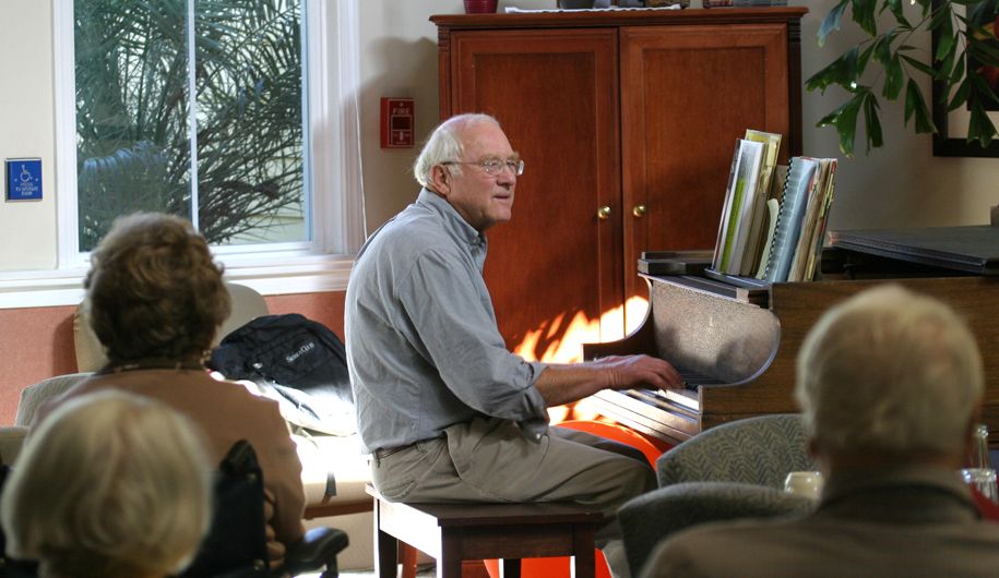 A man playing the piano indoors with sunlight streaming in.