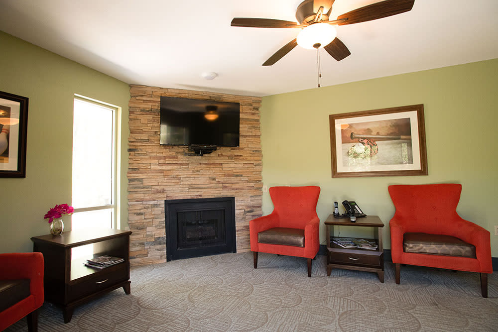 A cozy living room with red armchairs, a brick fireplace, and a mounted television.