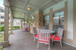 A covered patio with tables and chairs, featuring a stone wall and a relaxing atmosphere.