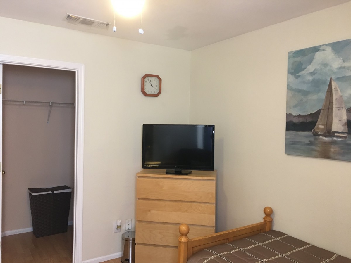 A bedroom with a television on a dresser, a clock on the wall, and a bed in the corner.