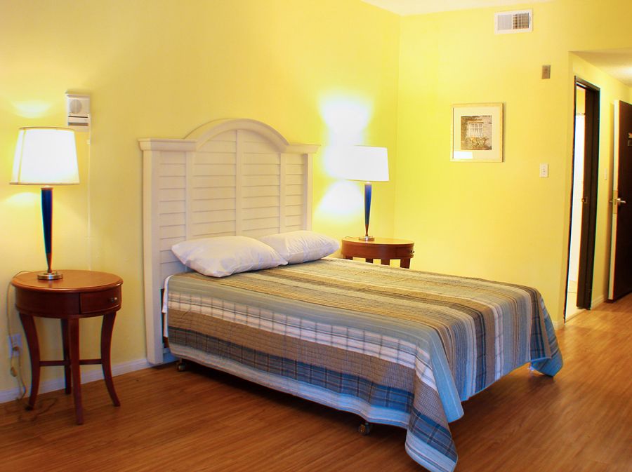 A cozy bedroom with yellow walls, featuring a bed, side table, and a lamp.