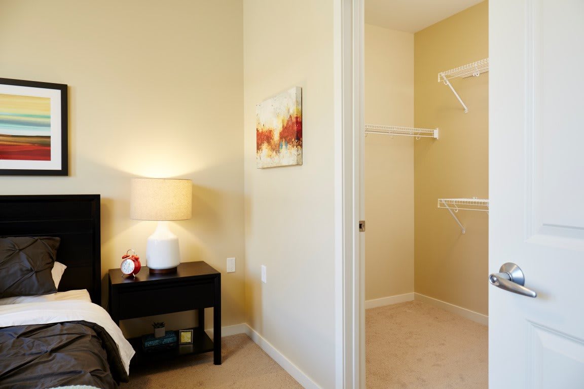 A cozy bedroom with a nightstand and lamp, featuring a small closet.