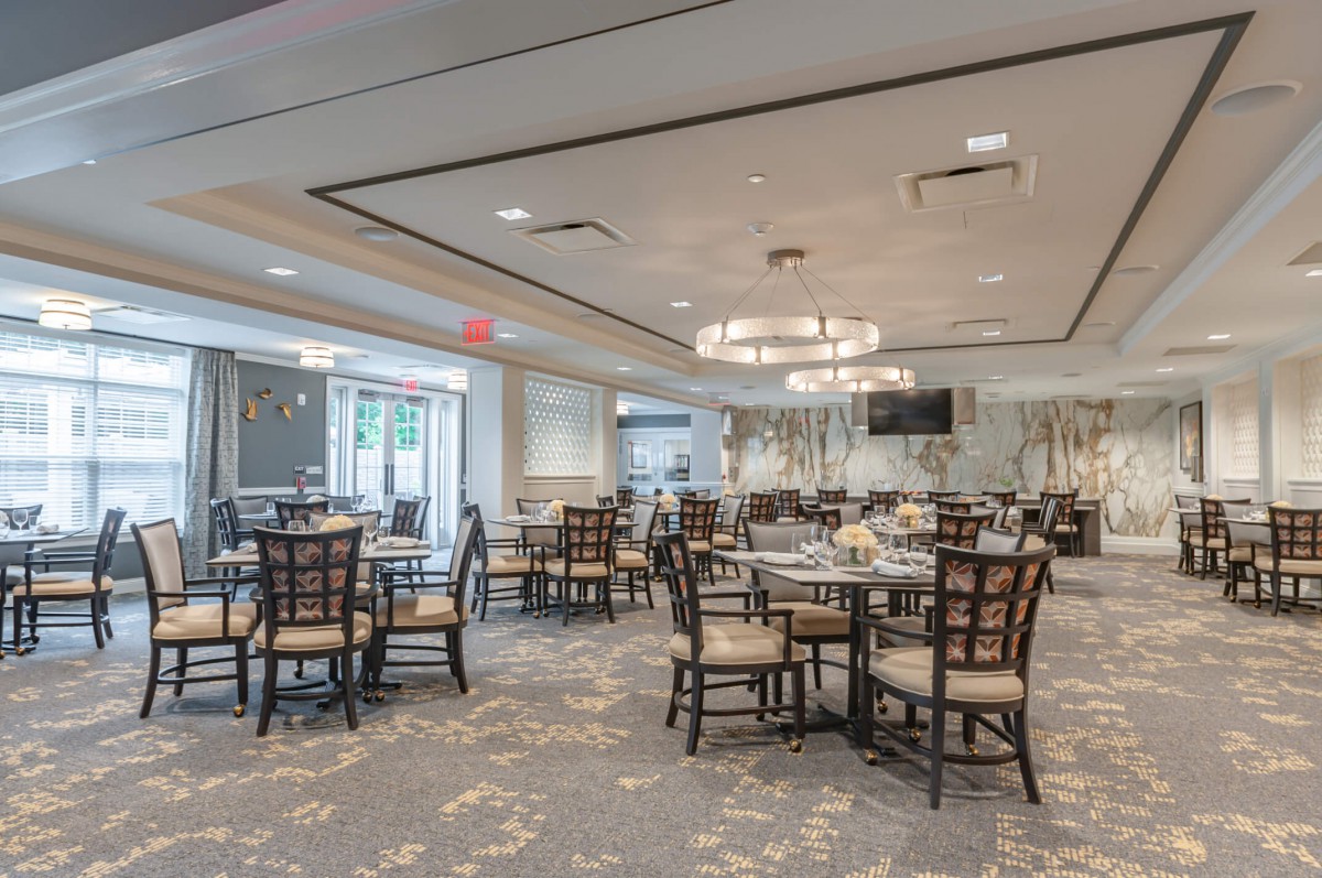 A spacious and elegantly decorated dining room with multiple tables and chairs, featuring modern chandeliers.