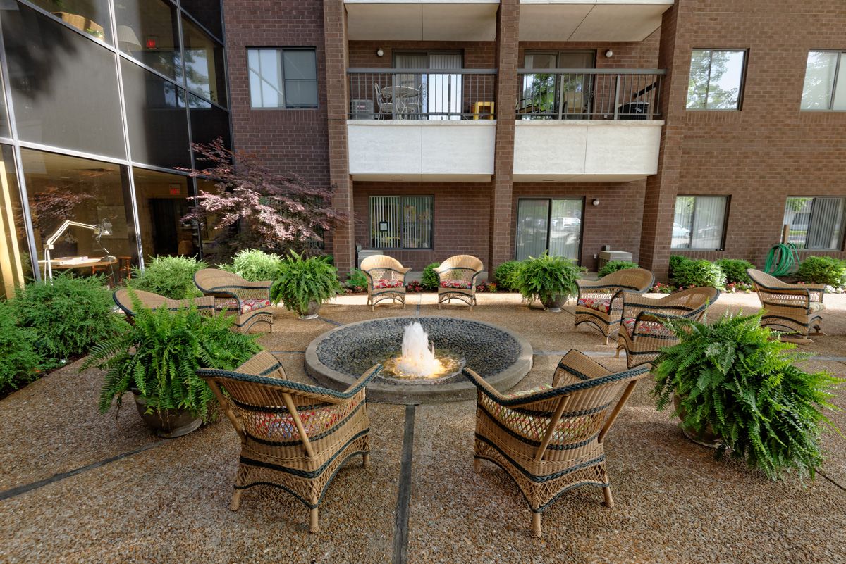 A cozy outdoor seating area with a central fountain surrounded by greenery, in front of an apartment building.