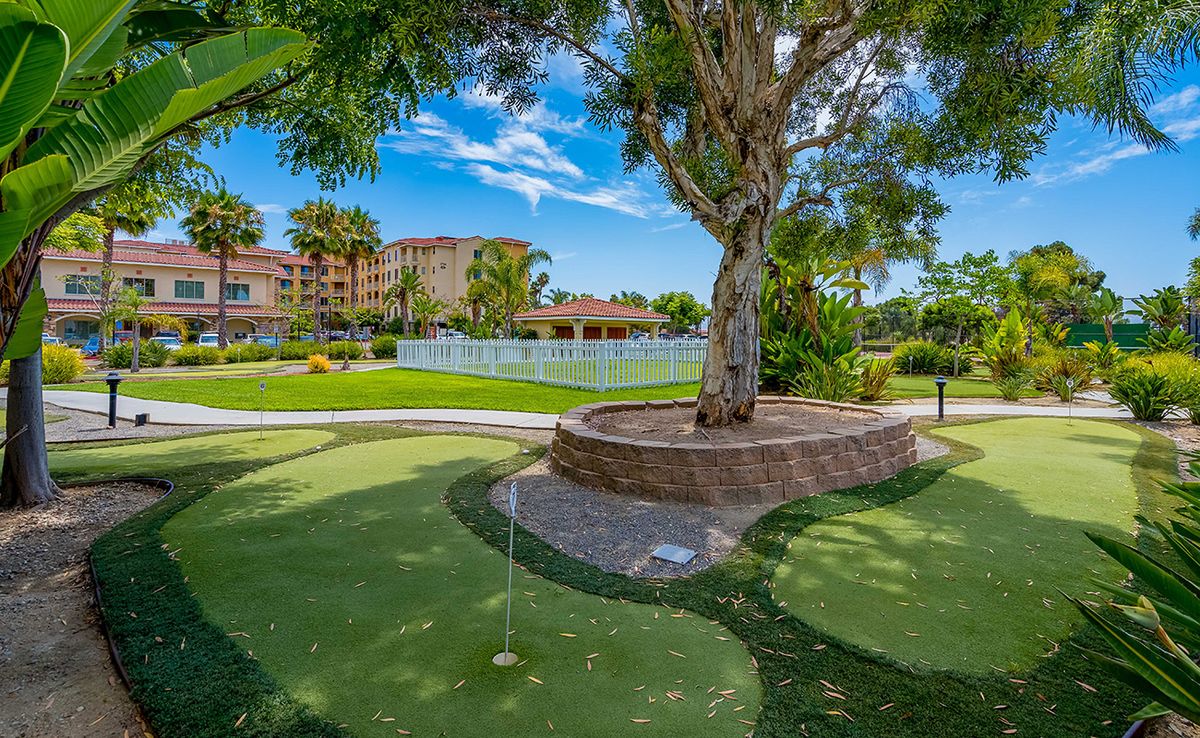 A scenic view of a golf course surrounded by lush greenery and resort buildings under a clear blue sky.