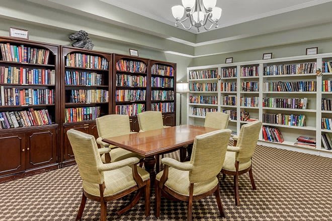 A cozy library room with bookshelves, a wooden table, and comfortable chairs.