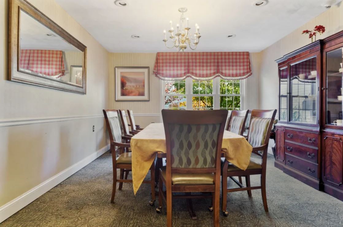 A cozy dining room with a large table, surrounded by chairs and illuminated by a chandelier.