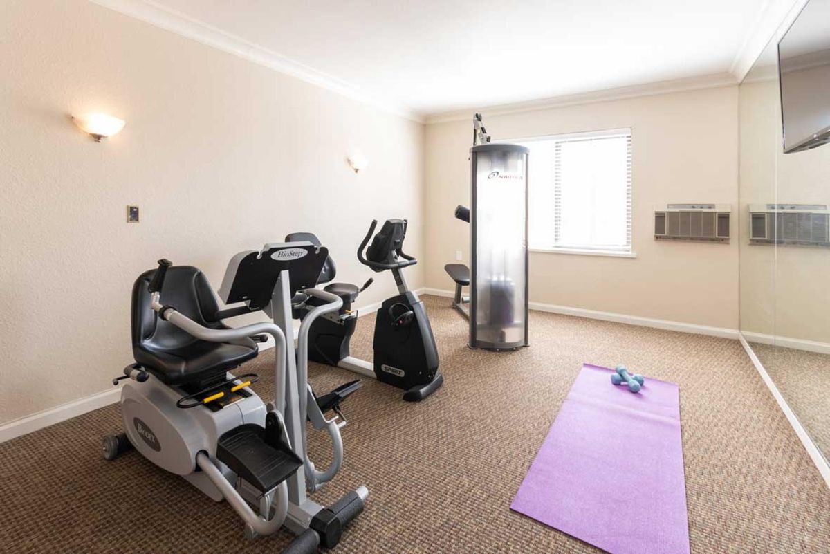A well-lit home gym with exercise bikes, a purple yoga mat, and dumbbells.