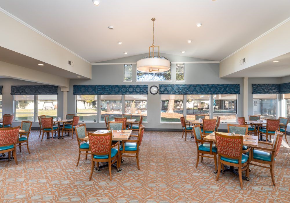 A spacious dining room with multiple tables and chairs, large windows, and a chandelier.