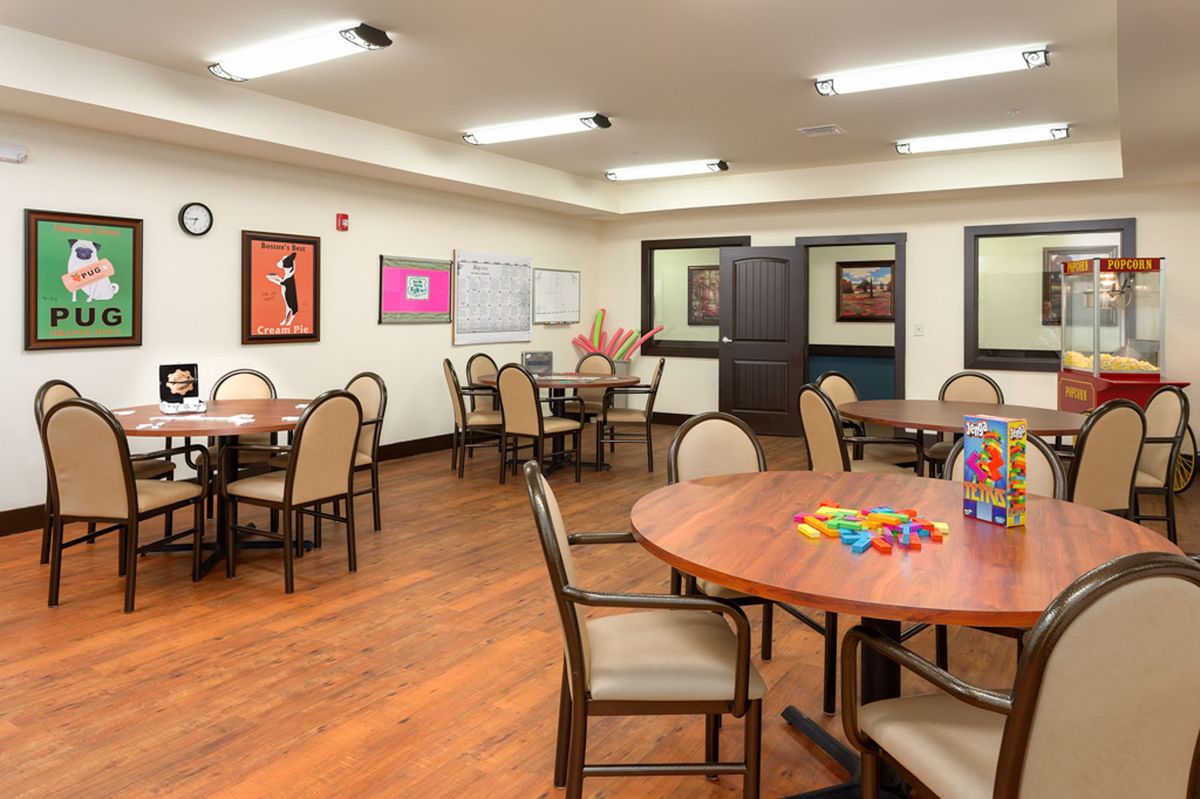 A community activity room with tables and chairs arranged for gatherings, featuring colorful artwork on the walls.