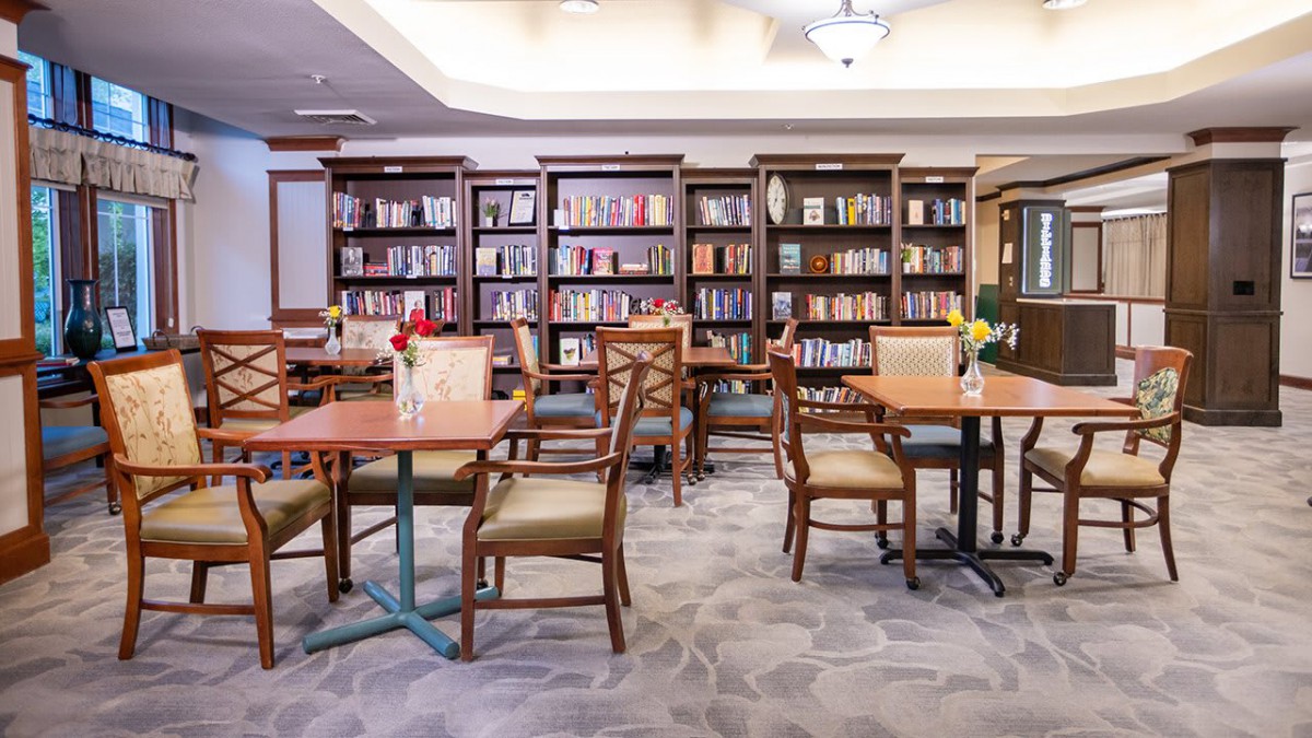 A cozy library with wooden tables and chairs, surrounded by bookshelves filled with books.