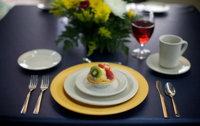 An elegantly set table with a fruit tart dessert and a glass of wine.