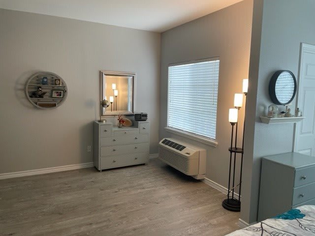 A modern, minimalist bedroom with a dresser, mirror, and standing lamp.