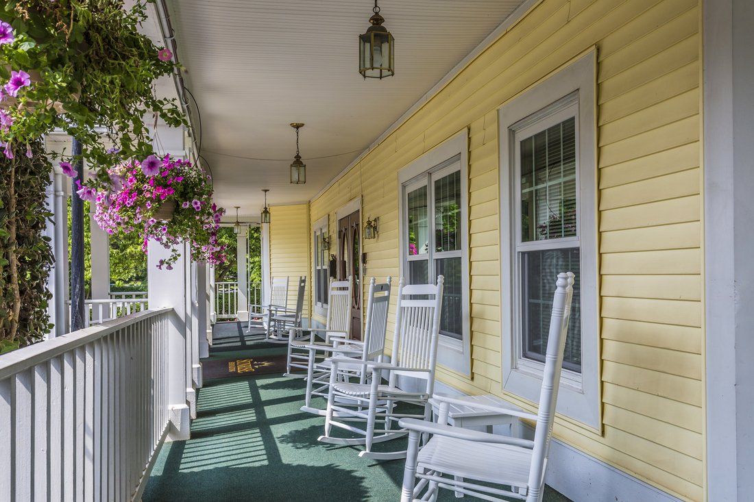 A charming yellow porch with white rocking chairs and hanging flowers on a sunny day.