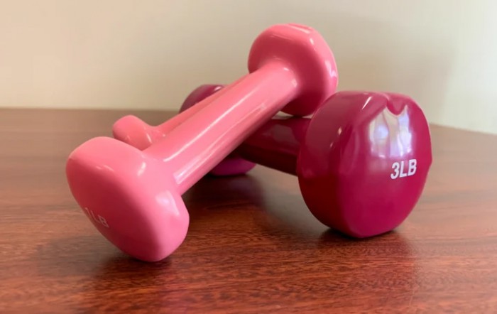 A pair of pink dumbbells resting on a wooden surface.