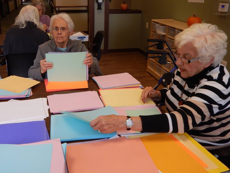 Elderly individuals engaging in a paper crafting activity at a table.