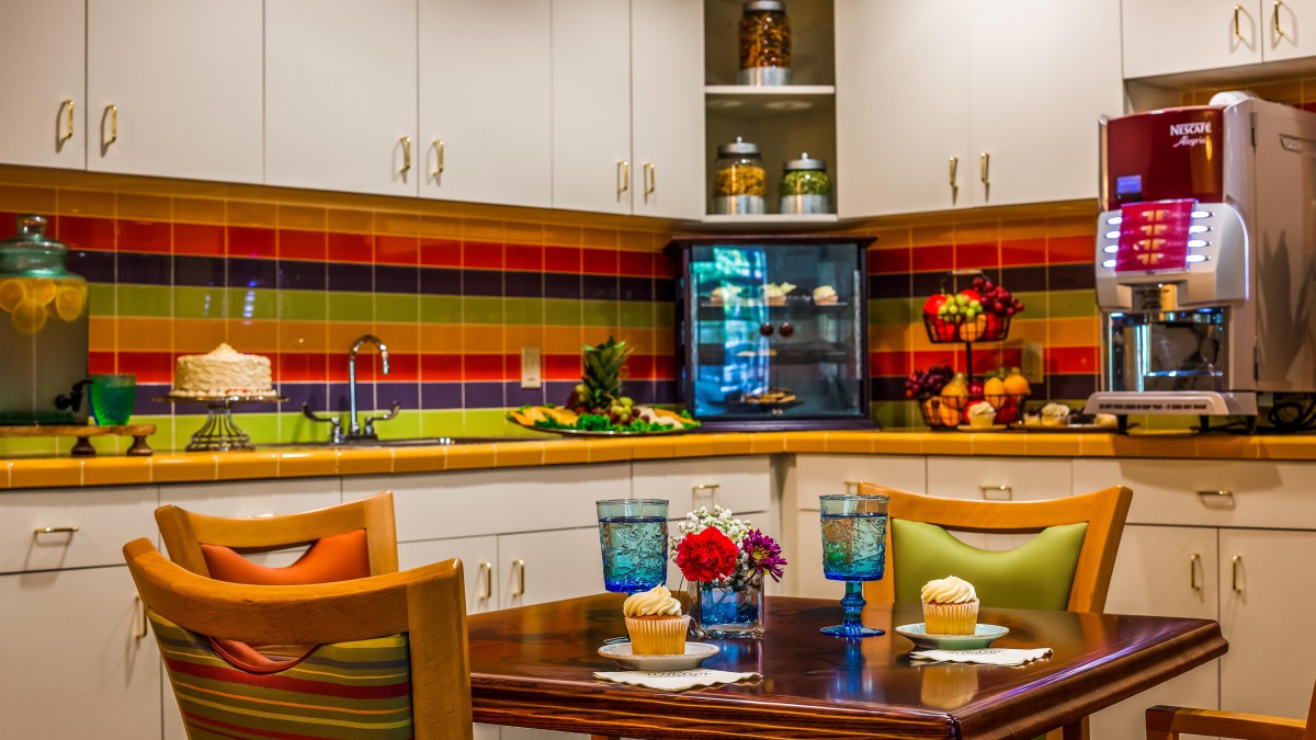 A modern kitchen with a colorful striped backsplash features a cozy seating area, complete with drinks, cupcakes, and decorative elements.