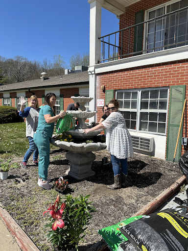 A group of volunteers working together to clean and maintain a garden fountain on a sunny spring day.