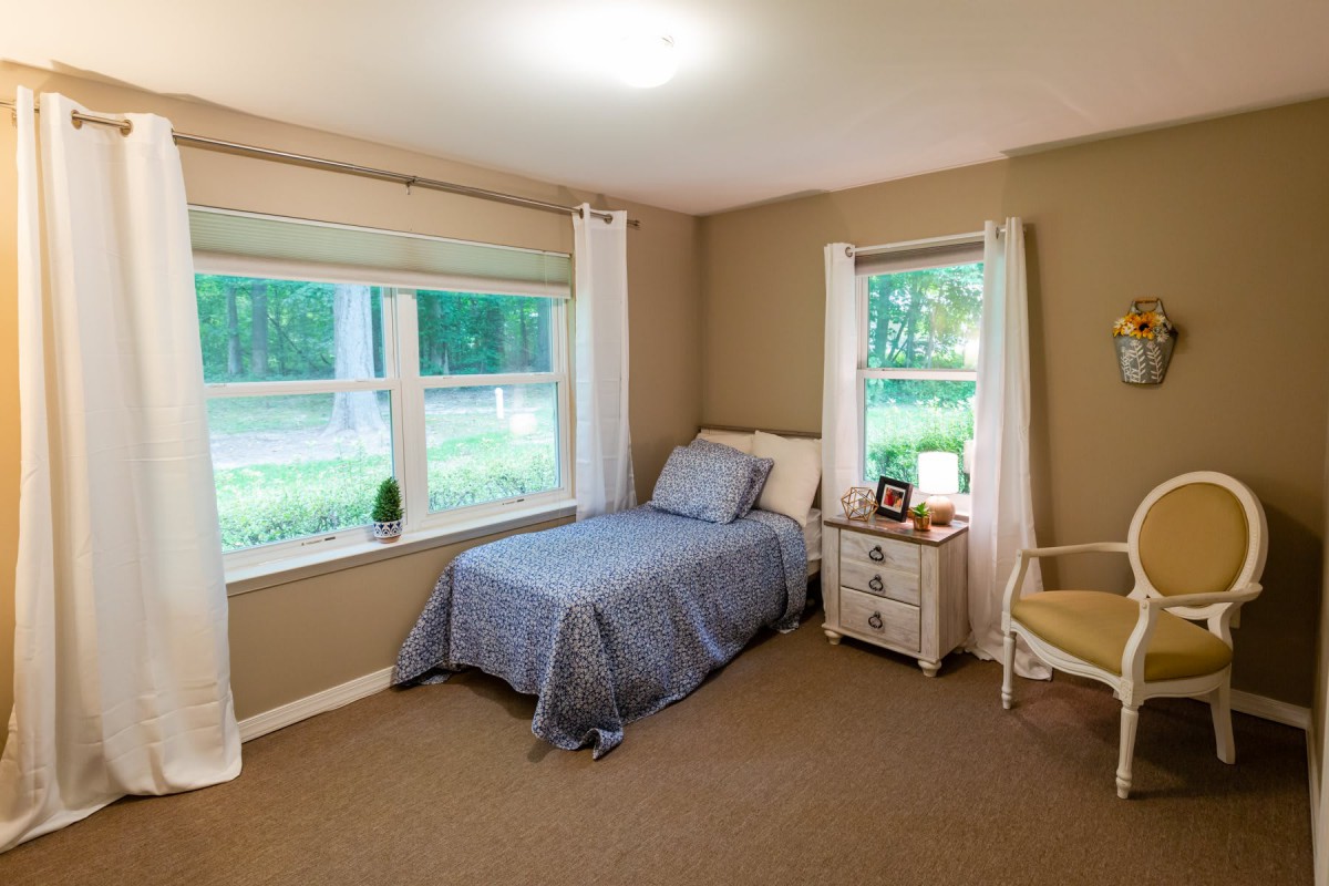 A cozy bedroom with a single bed and large windows overlooking a wooded area.