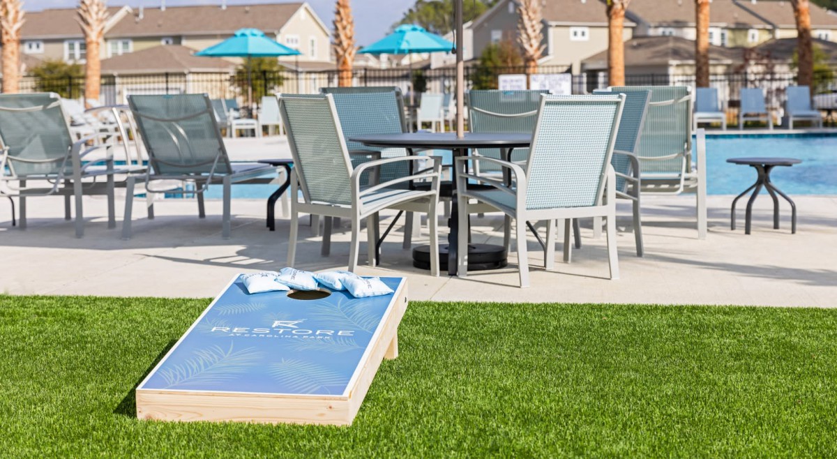 A relaxing poolside setup with patio furniture and a cornhole game on the lawn.