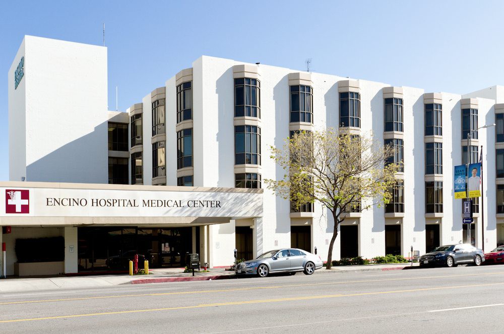 A view of a hospital and medical center building with a parking area in front.