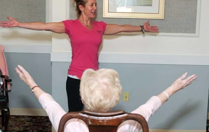 An instructor leads a seated exercise session for an elderly participant.