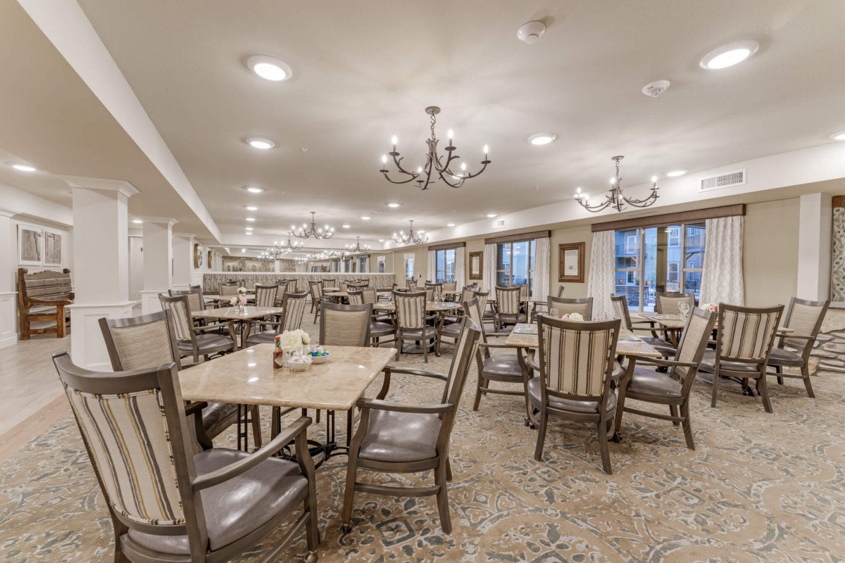 A spacious dining room with neatly arranged tables and chairs, illuminated by elegant chandeliers.