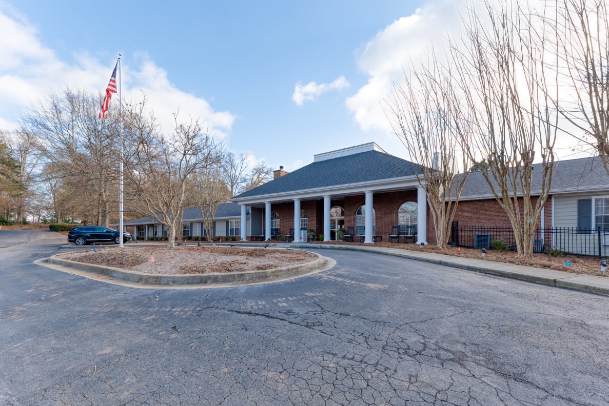 A building entrance with columns and an American flag in the parking lot.