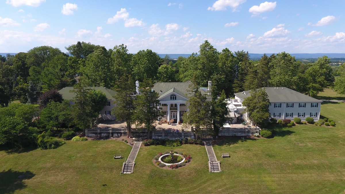 Aerial view of a grand mansion surrounded by trees and landscaped gardens.