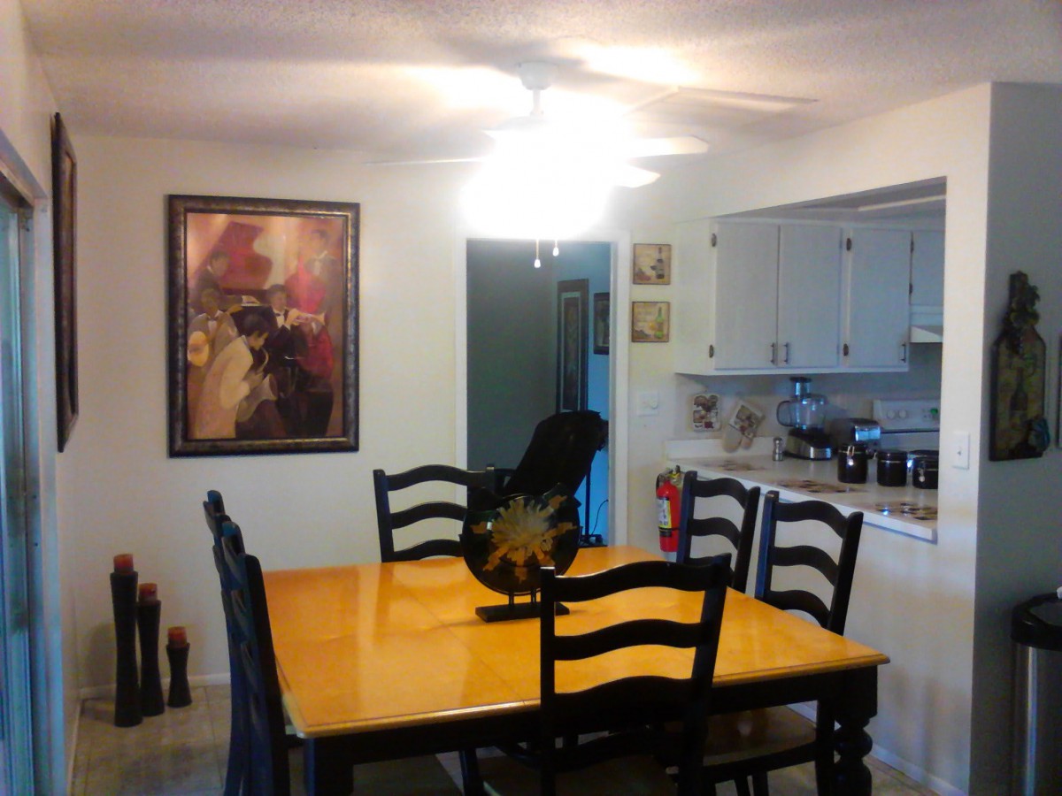 A cozy dining area with a wooden table and chairs, decorated with artwork on the wall, adjacent to a kitchen.