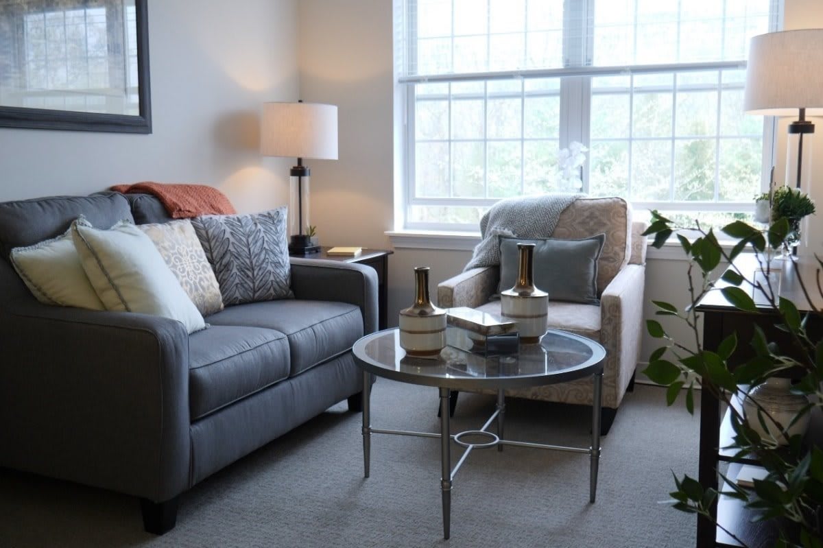 A cozy living room with a sofa, armchair, and coffee table near a large window.
