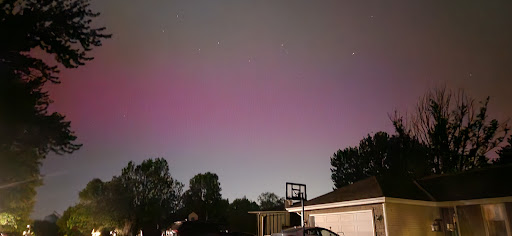 A mesmerizing display of purple hues in the night sky, captured from a backyard with a basketball hoop.
