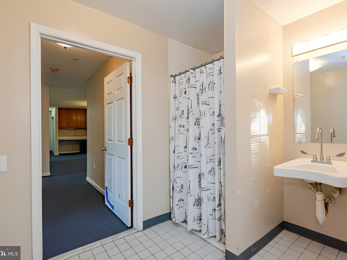 A clean bathroom with a shower curtain, sink, and doorway leading to a hallway.